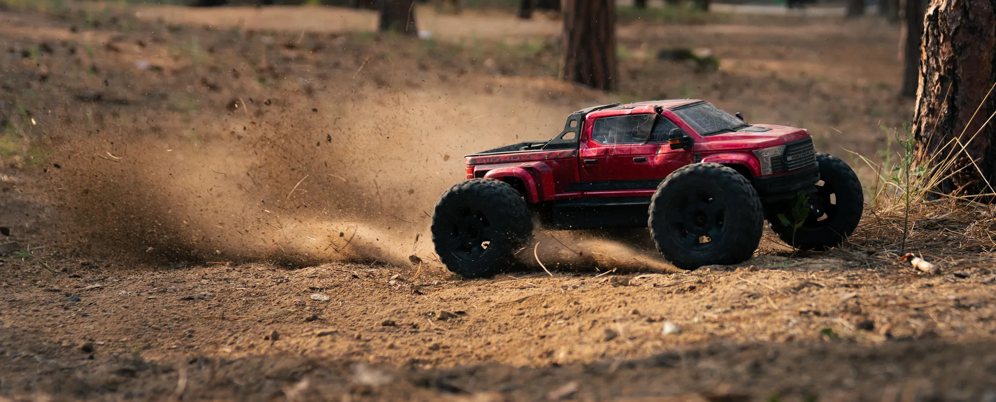 An RC monster truck kicking up dirt on a forest trail